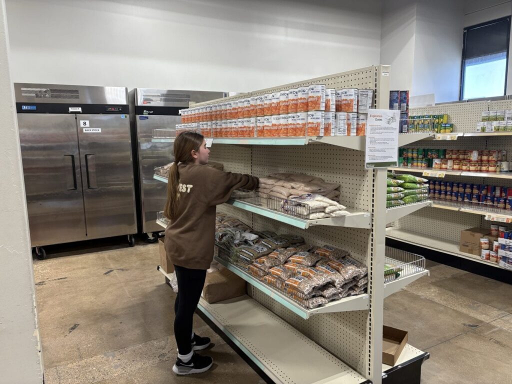 A person stocks shelves with canned food and dry goods in a grocery store or food pantry.