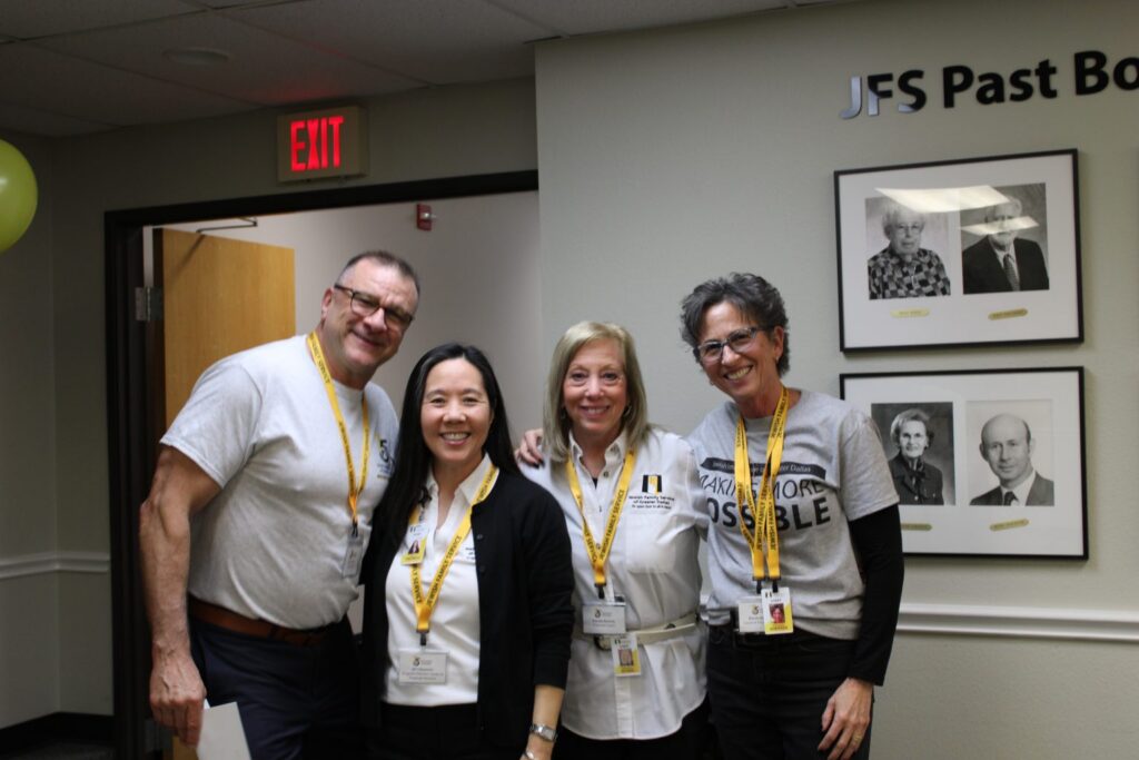 Four smiling adults with yellow lanyards stand together indoors in front of a wall with framed black-and-white photos.