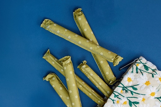 Six green-wrapped tampons spill out of a floral-patterned bag onto a blue surface.