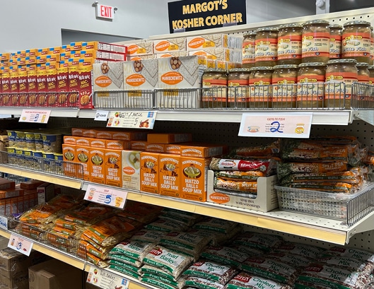 Shelves in a grocery store display kosher food items, including matzo ball mix, soup mix, pretzels, and jars of sauce.
