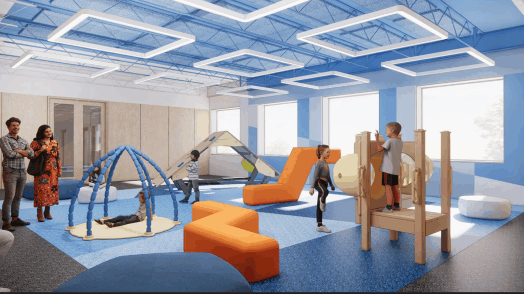 Children play on colorful equipment in a bright, modern indoor playroom with adults observing nearby.