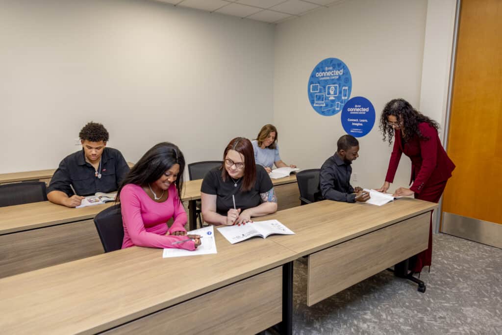 Students sit at desks reading while a teacher assists in a classroom with a “connected” sign on the wall.