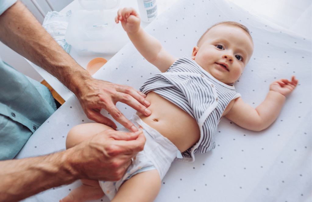 An adult changes a smiling baby’s diaper on a changing table with a white polka dot cover.