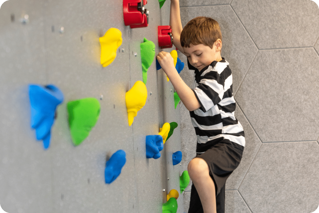 A child climbs a colorful rock wall in the JFS Dallas sensory gym.