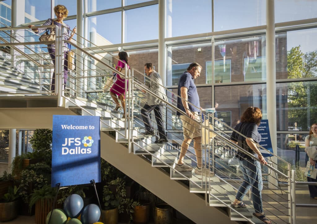 People walking up a staircase next to a sign for JFS Dallas.